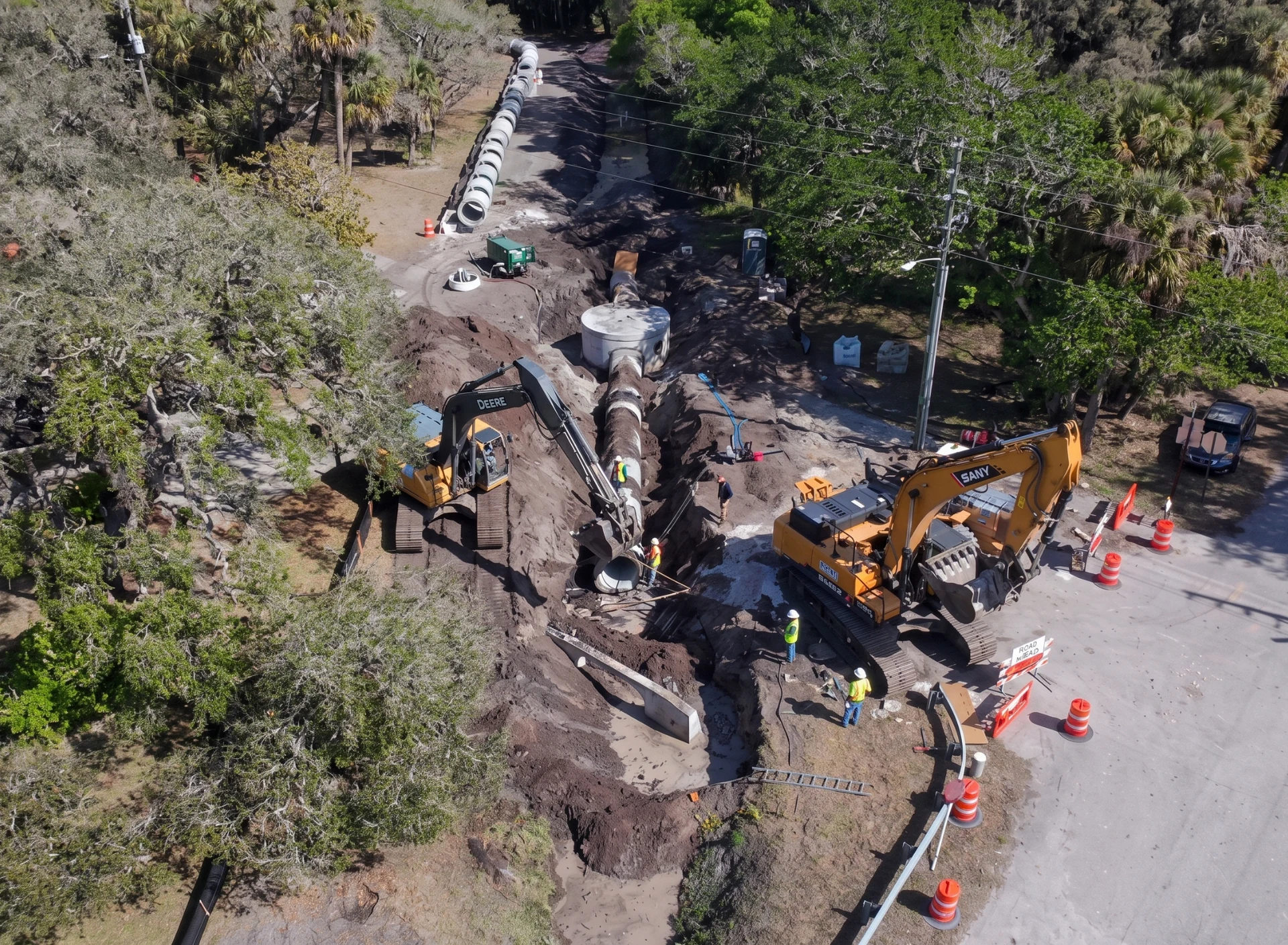Excavation beside a road with equipment and pipe sections staged for drainage installation